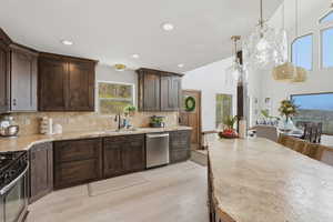 Kitchen with dark wood finish cabinets, decorative light fixtures, light wood-type flooring, stainless steel appliances, and light stone countertops