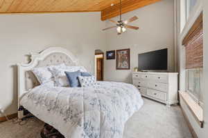 Bedroom featuring light carpet, ceiling fan, a high wood beamed ceiling, and arched walkways