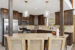 Kitchen featuring dark wood finish cabinets, a kitchen breakfast bar, stainless steel appliances, light stone counters, and backsplash