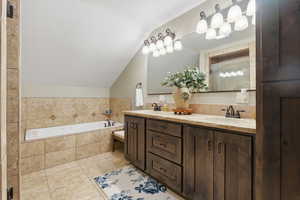 Bathroom with double vanity, a bath, vaulted ceiling, and light tile patterned floors