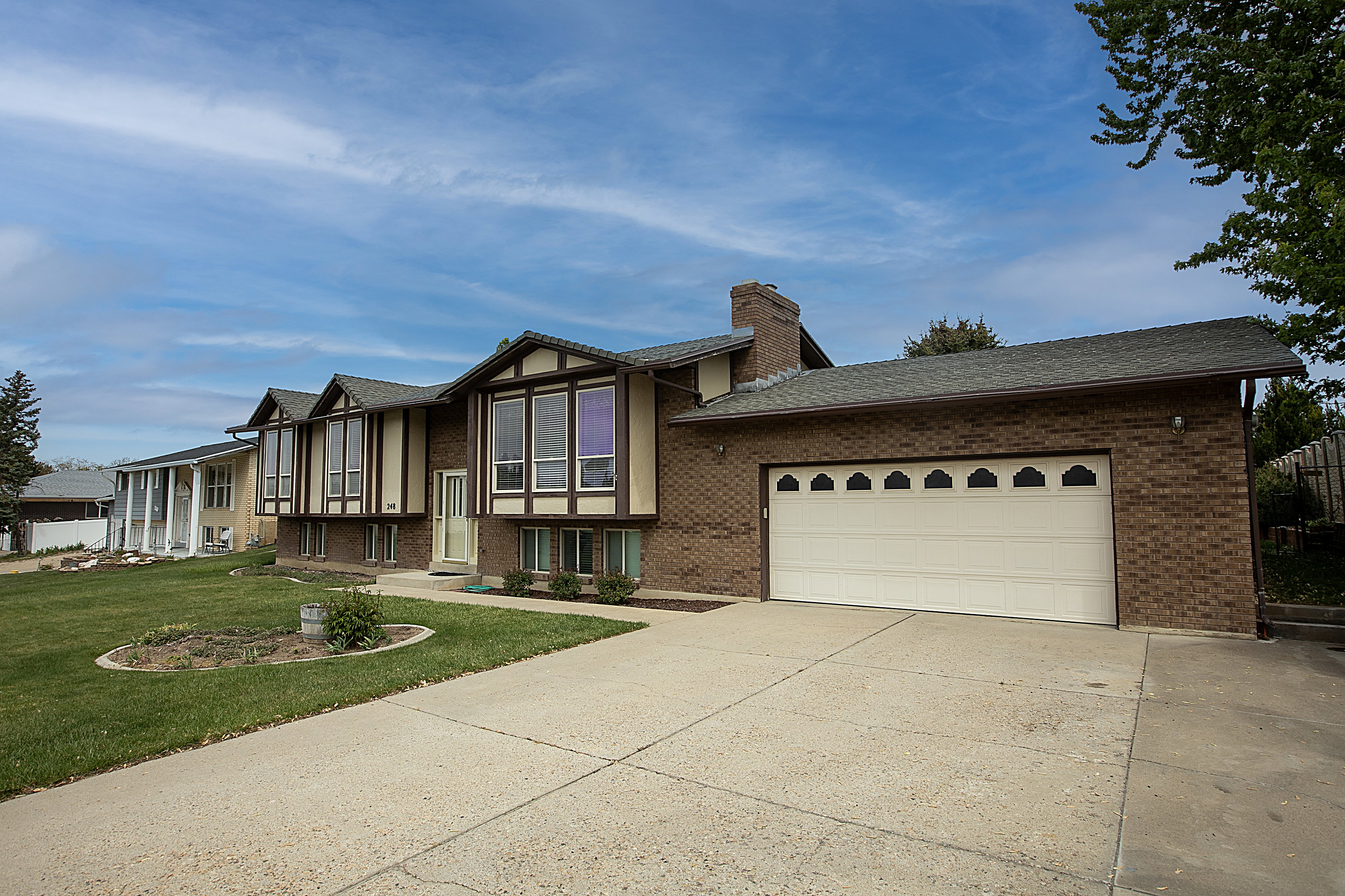 Bi-level home with a garage, driveway, brick siding, and a front lawn