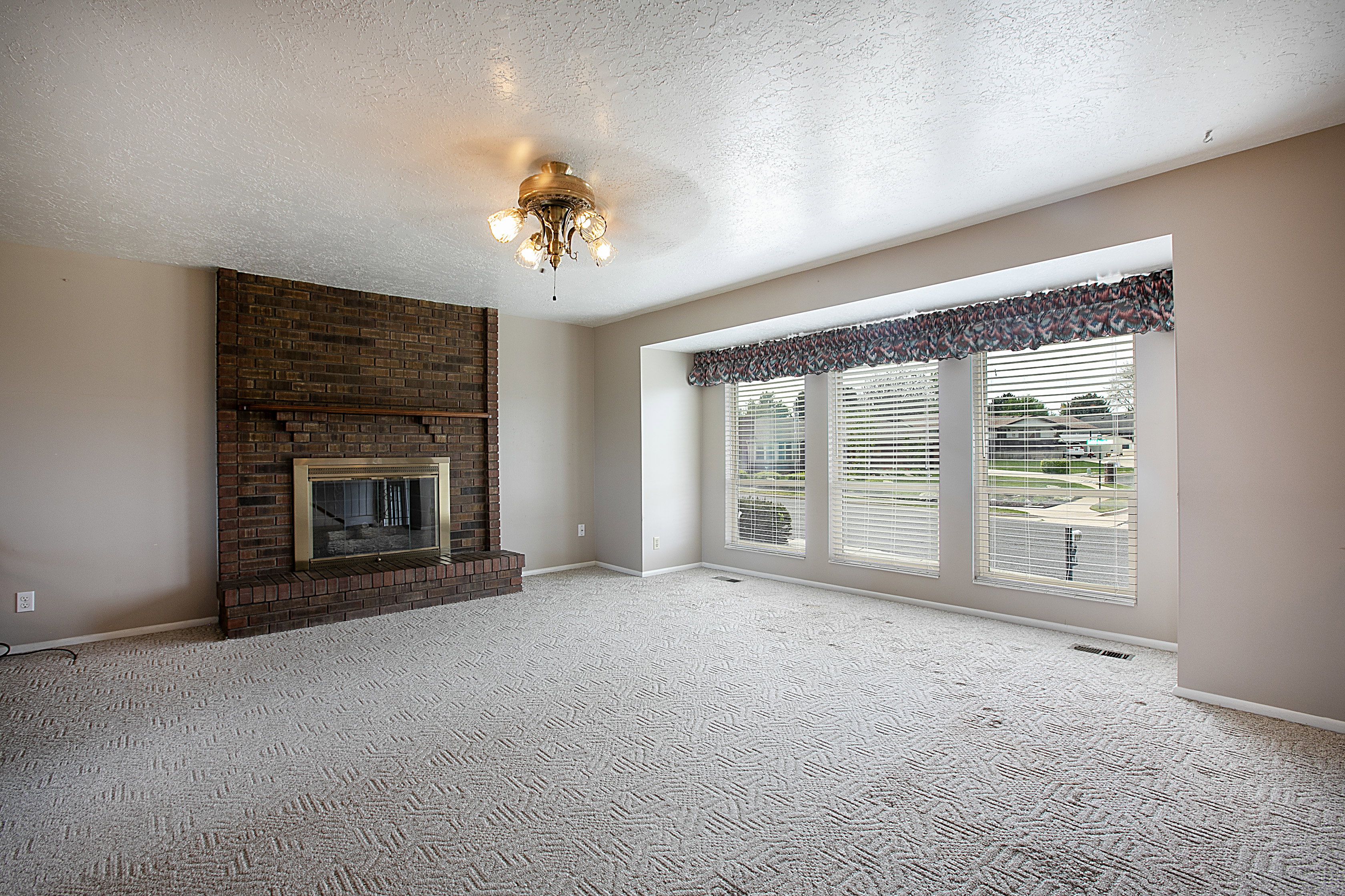Unfurnished living room featuring a brick fireplace, a textured ceiling, carpet flooring, and a ceiling fan
