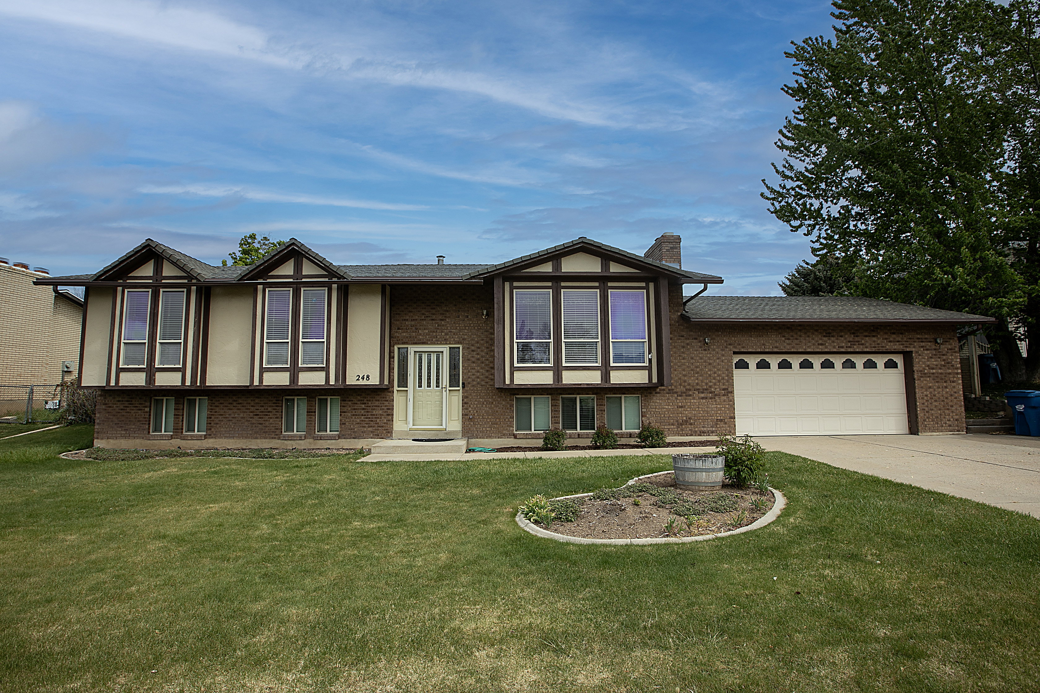 View of front of home featuring an attached garage, brick siding, a front lawn, concrete driveway, and a chimney