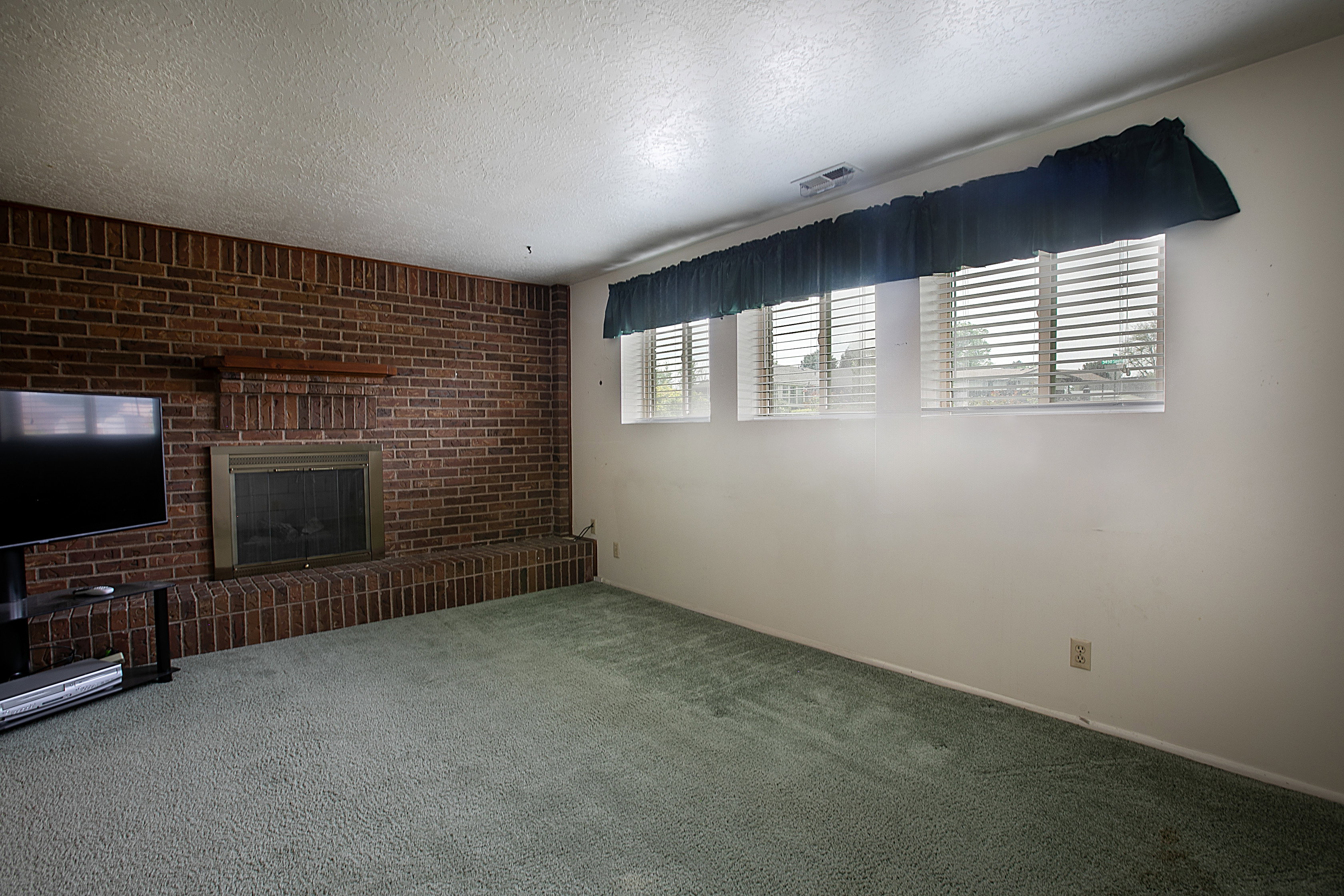 Unfurnished living room with brick wall, carpet flooring, a fireplace, and a textured ceiling