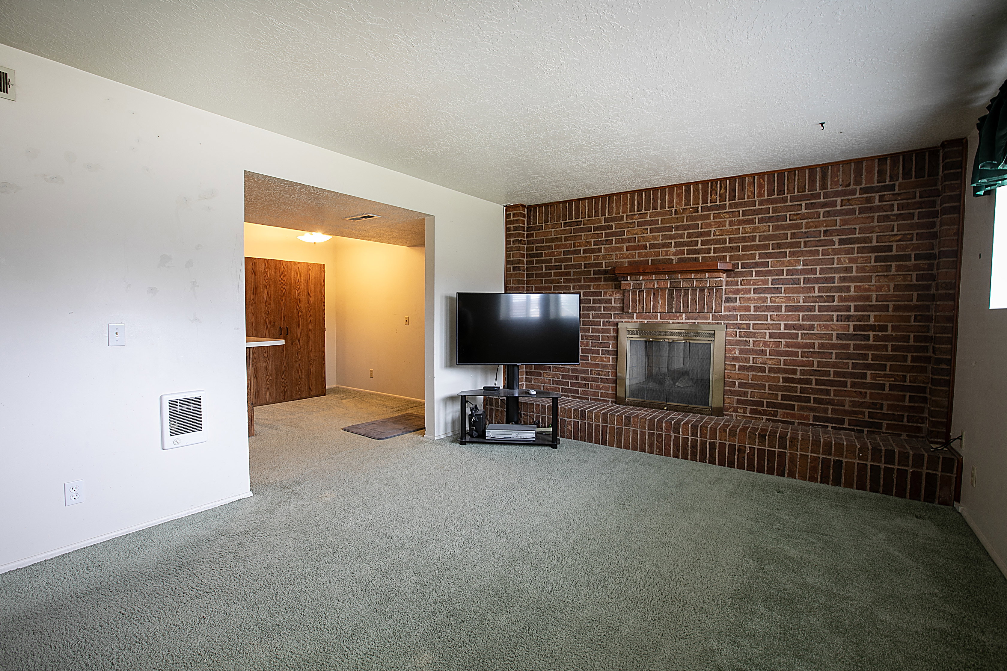 Unfurnished living room featuring brick wall, a textured ceiling, carpet, and a fireplace