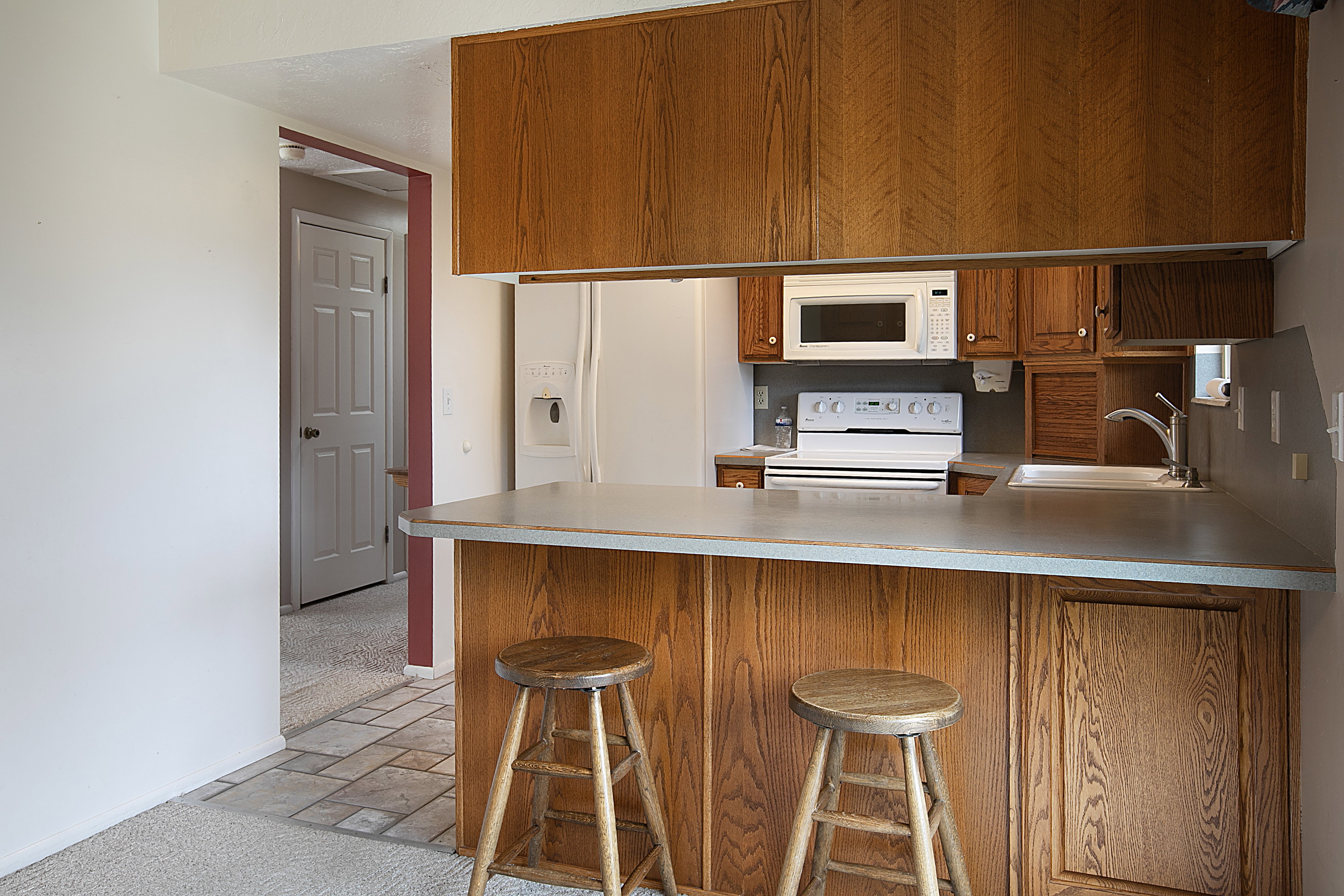 Kitchen with a peninsula, white appliances, light countertops, stone tile floors, and wood finish cabinets