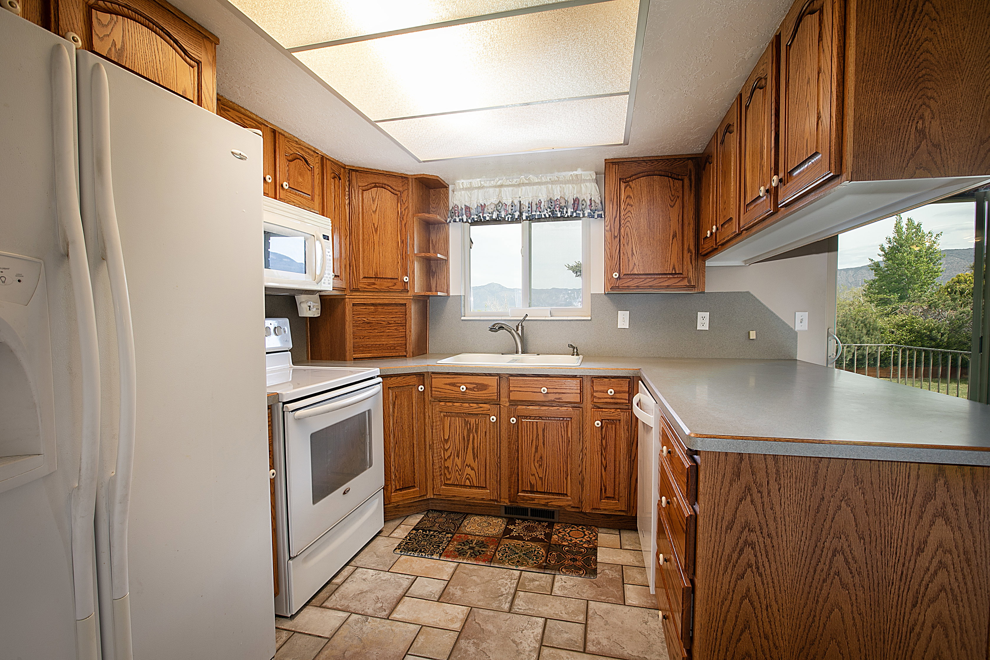 Kitchen featuring wood finish cabinetry, white appliances, light stone finish floors, and open shelves