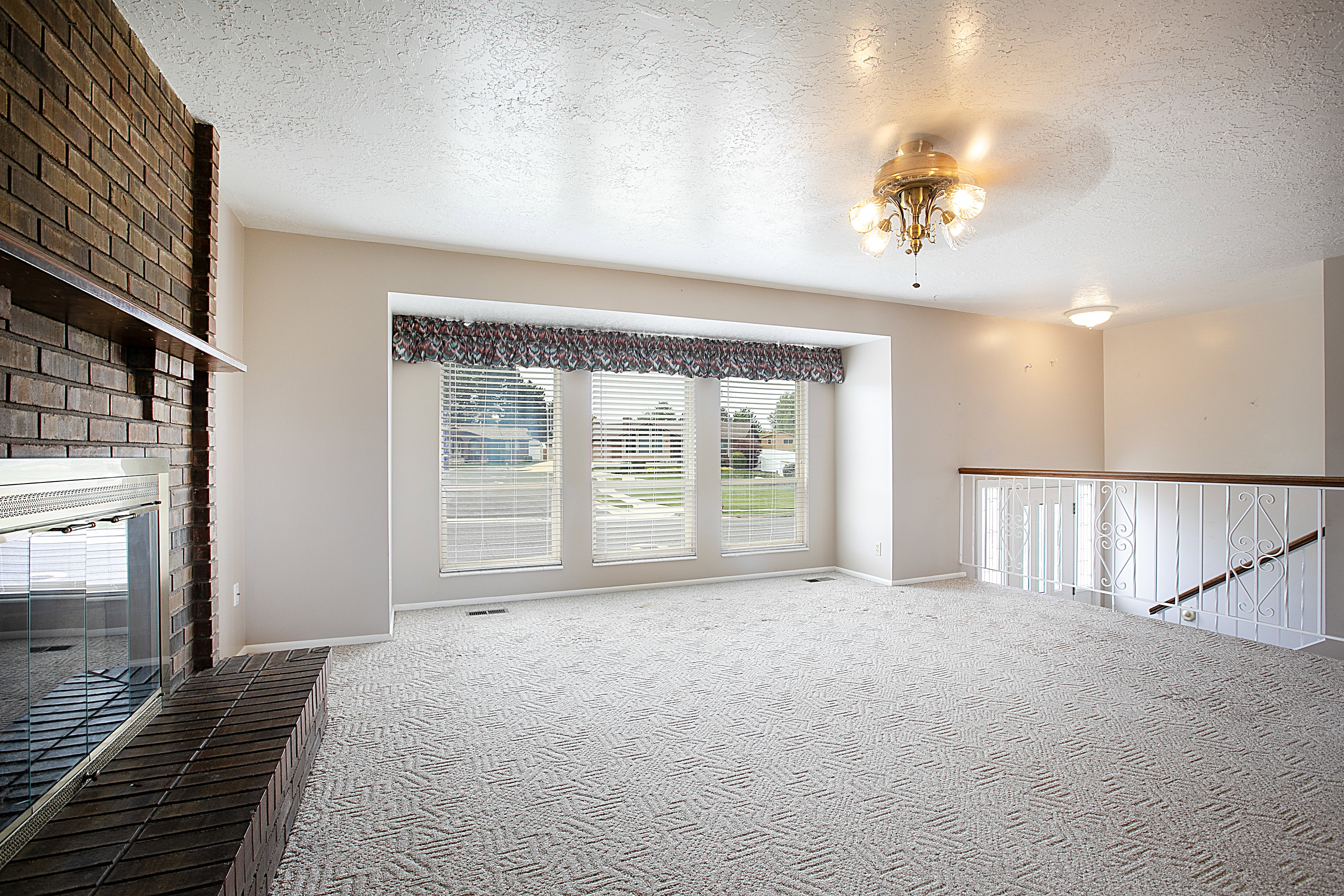 Unfurnished living room with carpet floors, a textured ceiling, and a brick fireplace