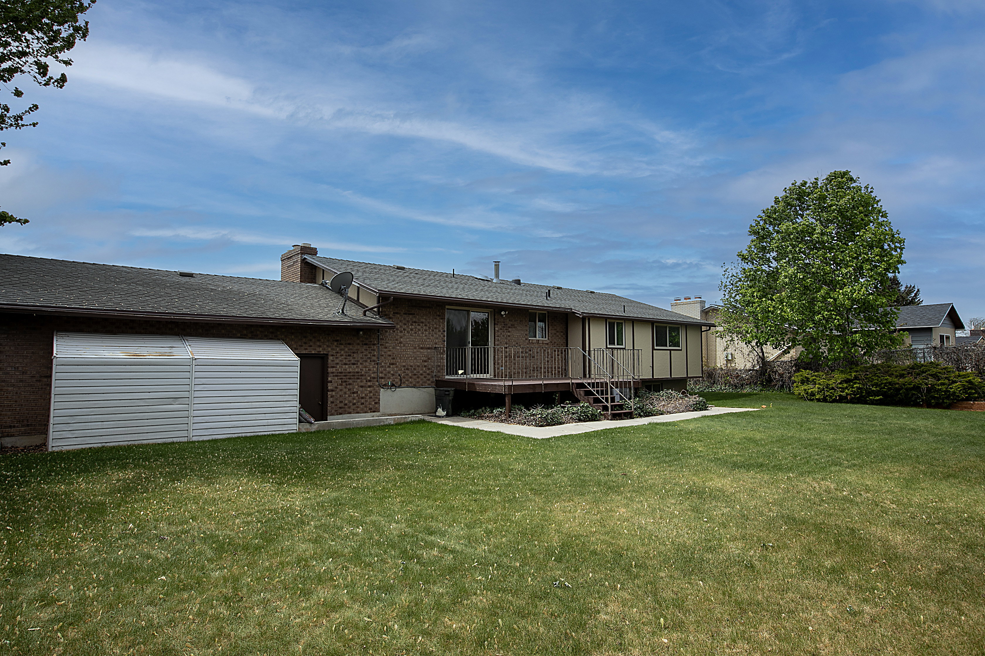 Back of property with brick siding, a deck, a chimney, and roof with shingles