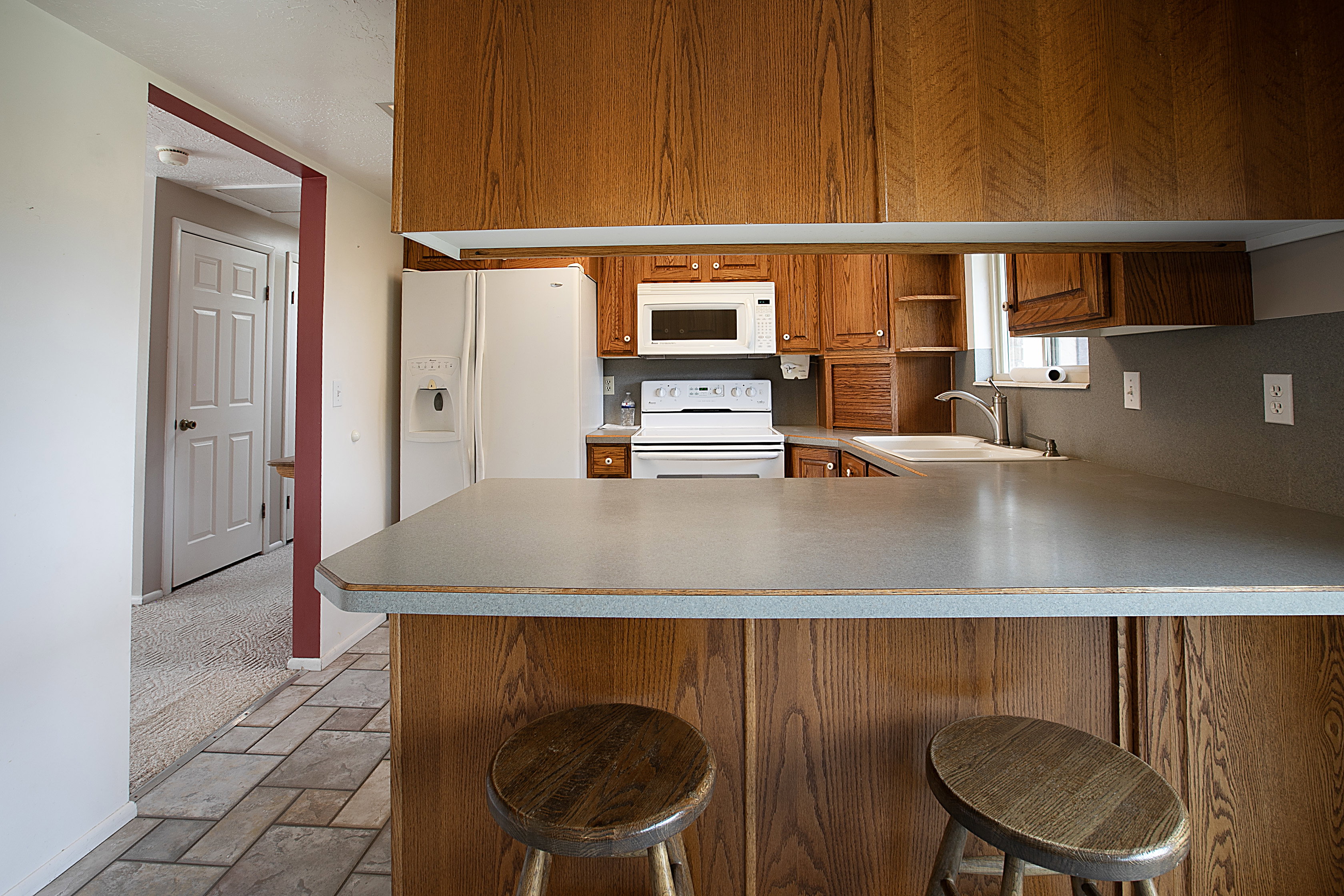 Kitchen featuring a peninsula, white appliances, a kitchen breakfast bar, and light countertops