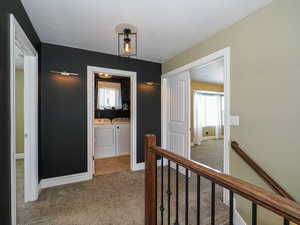 Hall with light carpet, washing machine and clothes dryer, a textured ceiling, and an upstairs landing
