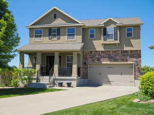View of front of property featuring a porch, stucco siding, concrete driveway, stone siding, and an attached garage