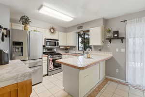 Kitchen featuring stainless steel appliances, a peninsula, light tile patterned floors, white cabinetry, and open shelves