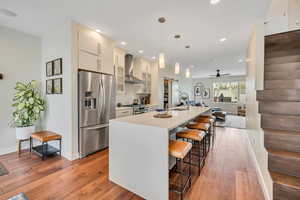 Kitchen with stainless steel appliances, a breakfast bar, a large island, light stone counters, and light wood-style flooring