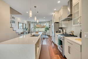 Kitchen with glass fronted cabinets, stainless steel range with gas stovetop, dark wood finished floors, white cabinetry, and hanging light fixtures
