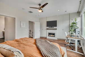 Master Bedroom featuring multiple closets, a glass covered fireplace, recessed lighting, hardwood / wood-style flooring, and a desk