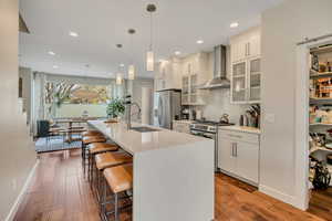 Kitchen featuring glass fronted cabinets, a kitchen bar, stainless steel appliances, white cabinets, and light wood finished floors