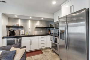 Kitchen featuring white cabinetry, stainless steel appliances, open shelves, recessed lighting, and dark countertops