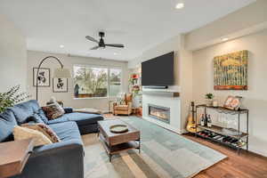Living area featuring a ceiling fan, recessed lighting, wood finished floors, and a glass covered fireplace