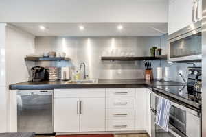 Kitchen featuring open shelves, white cabinetry, stainless steel appliances, dark countertops, and recessed lighting