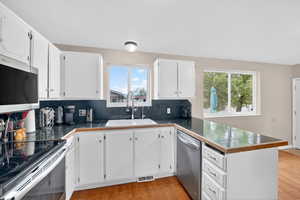 Kitchen with stainless steel appliances, light wood finished floors, white cabinetry, tasteful backsplash, and a peninsula
