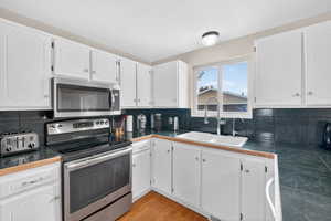 Kitchen featuring stainless steel appliances, white cabinets, decorative backsplash, light wood-style flooring, and tile countertops
