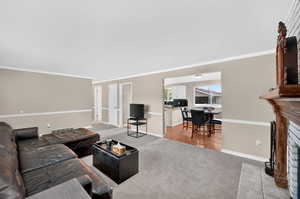 Living area with a fireplace, ornamental molding, and light carpet