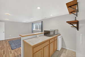 Kitchen featuring a peninsula, tile counters, light wood finish cabinetry, recessed lighting, and stainless steel microwave