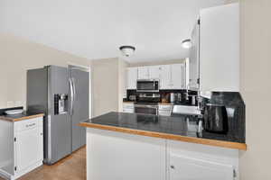 Kitchen with stainless steel appliances, white cabinets, light wood-type flooring, a peninsula, and tasteful backsplash