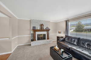 Carpeted living room featuring a brick fireplace and crown molding