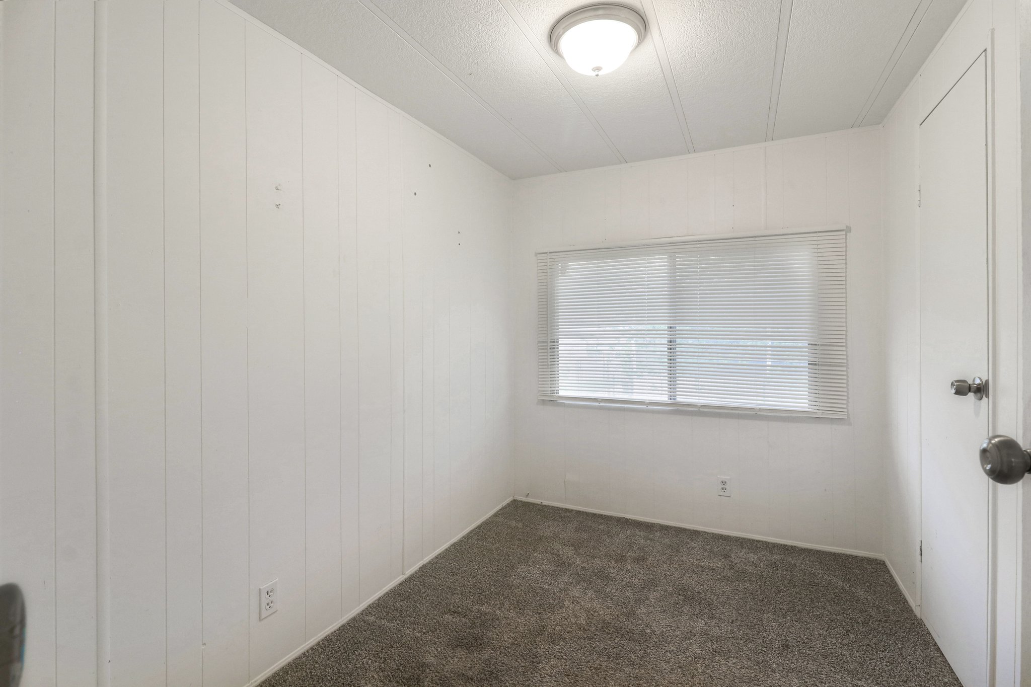 Empty room with dark carpet, wooden walls, and a textured ceiling
