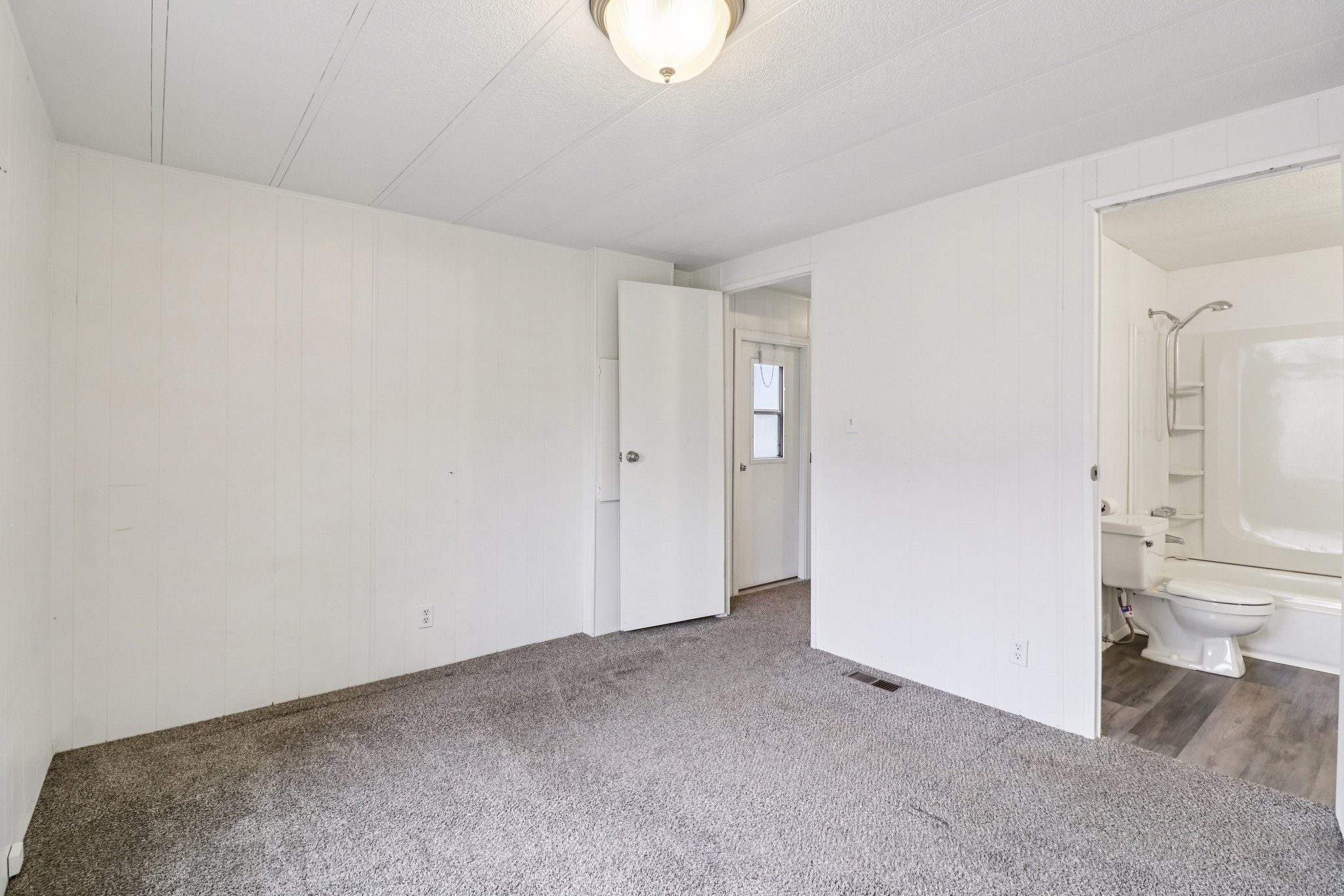 Unfurnished bedroom with carpet floors, ensuite bath, and wood walls