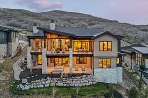 Rear view of house featuring a patio, a chimney, a balcony, a mountain view, and stone siding