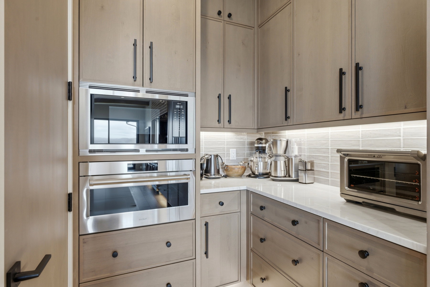 Kitchen featuring stainless steel appliances, decorative backsplash, light wood finish cabinets, and light stone counters
