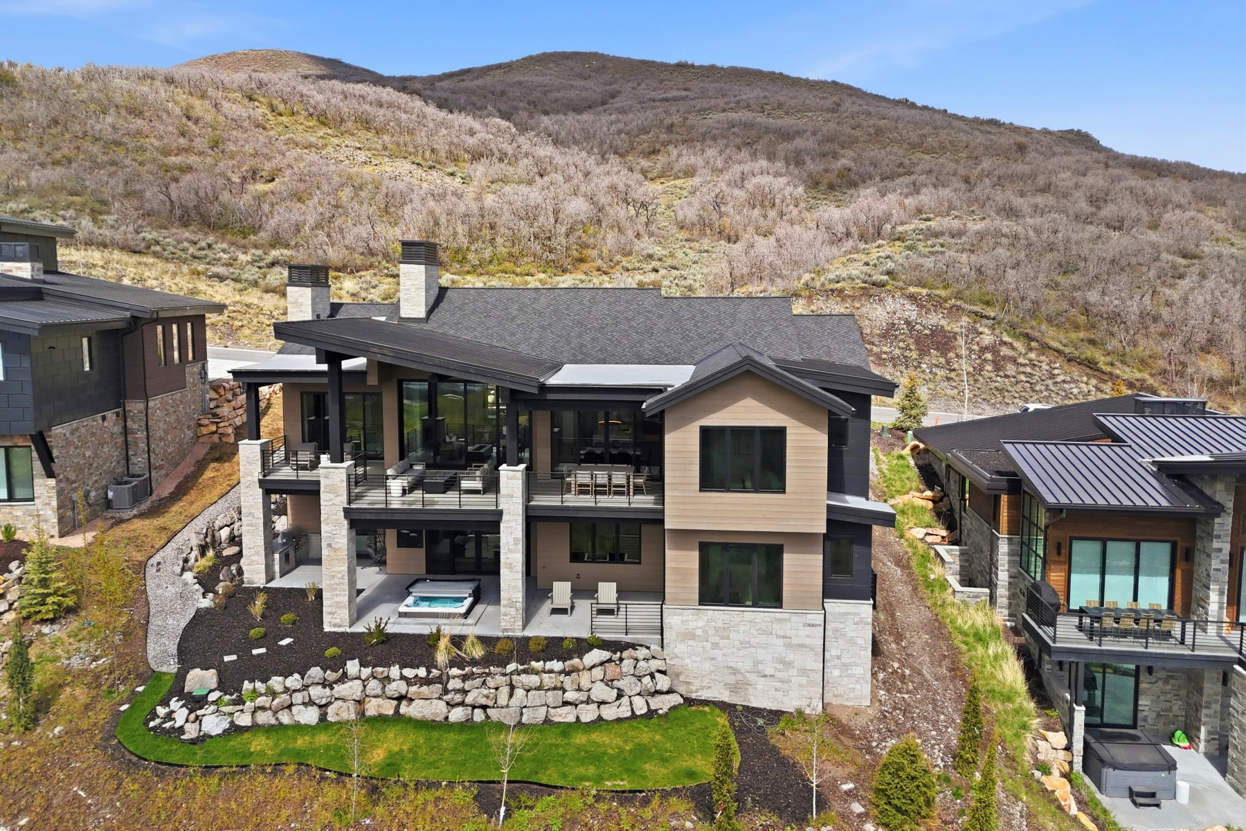 Rear view of property with stone siding, an outdoor hot tub, a mountain view, a chimney, and a patio