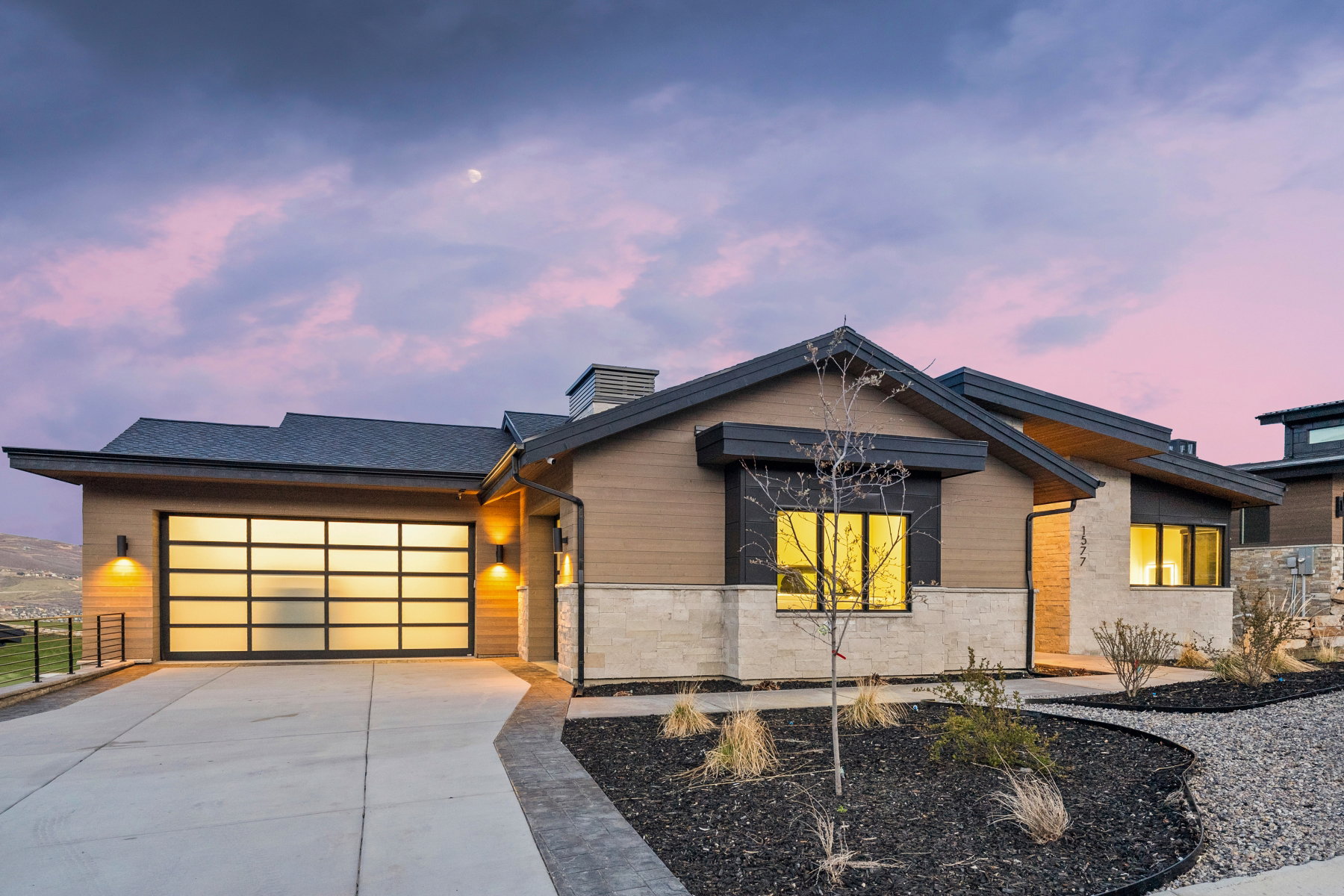Modern home with a garage, concrete driveway, stone siding, and a chimney