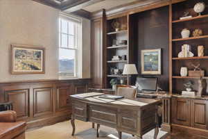 Home office with wallpapered walls, wainscoting, light wood-type flooring, built in features, and beamed ceiling