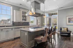 Kitchen with crown molding, a breakfast bar area, a kitchen island, island exhaust hood, and light stone counters