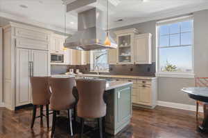Kitchen featuring ornamental molding, a kitchen bar, dual tone cabinets, island exhaust hood, and backsplash