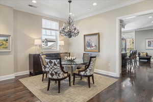 Dining space featuring crown molding, dark wood-style floors, healthy amount of natural light, and suspended lighting