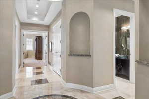 Hall with a raised ceiling and light marble finish floors