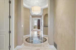 Hall featuring a tray ceiling, arched walkways, and light marble finish flooring
