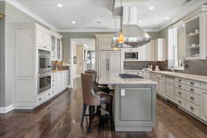 Dual tone kitchen featuring glass insert cabinets, hanging light fixtures, a center island, ornamental molding, and a kitchen bar