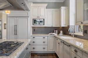 Kitchen with stainless steel appliances, light stone counters, dark wood-style floors, ornamental molding, and white cabinets