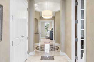 Foyer entrance with arched walkways, ornamental molding, a raised ceiling, and light marble finish flooring