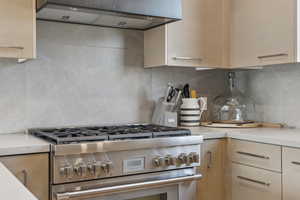 Kitchen with extractor fan, high end stainless steel range, decorative backsplash, and light wood finish cabinets