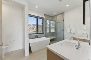 Bathroom featuring double vanity, a shower stall, a freestanding tub, light tile patterned flooring, and recessed lighting