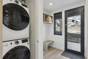 Laundry area featuring light wood finished floors, stacked washing machine and dryer, and recessed lighting