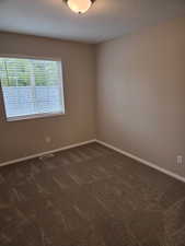 Empty room featuring dark carpet and baseboards