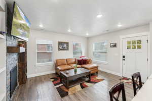 Living room with LVP flooring, a stone fireplace, recessed lighting, and a textured ceiling